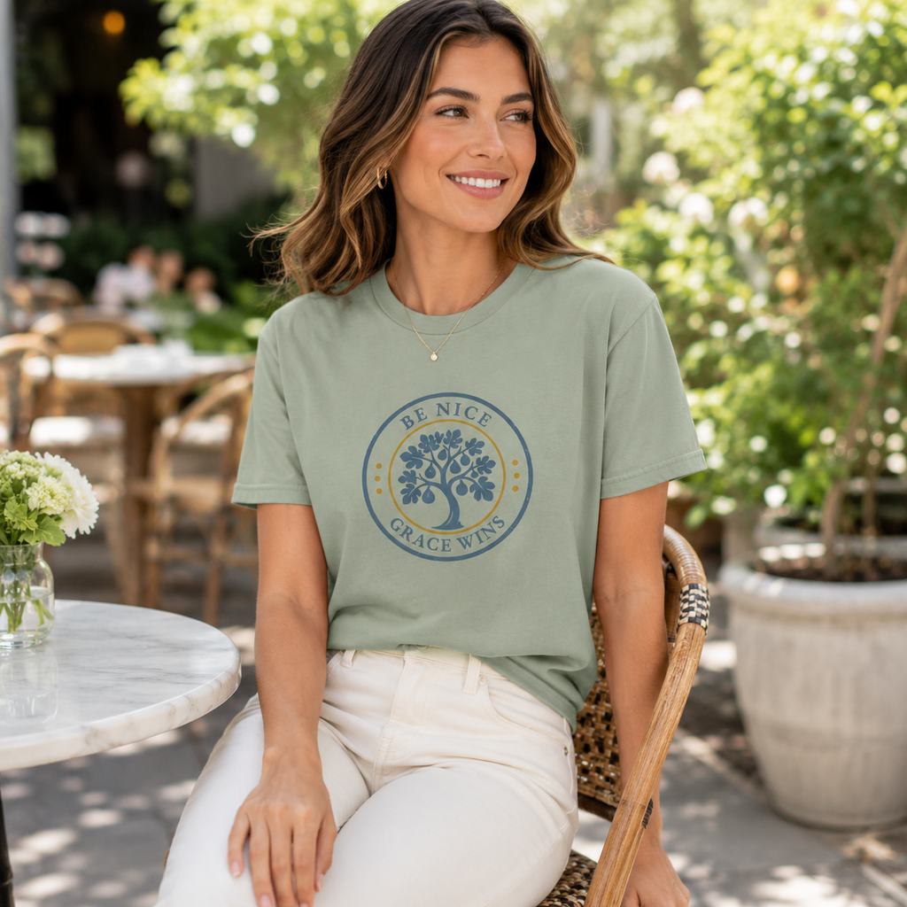 Woman wearing the Heritage Badge Tee in Sage at an outdoor cafe